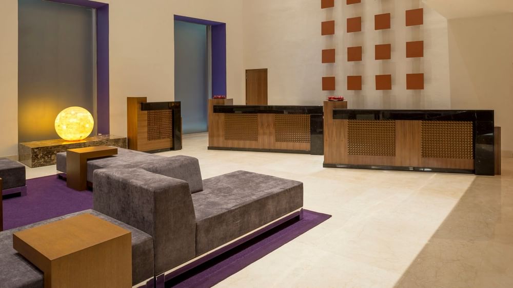 Lobby moderno de hotel en Camino Real Pedregal México con alfombras moradas, sofás grises y escritorios de madera elegante