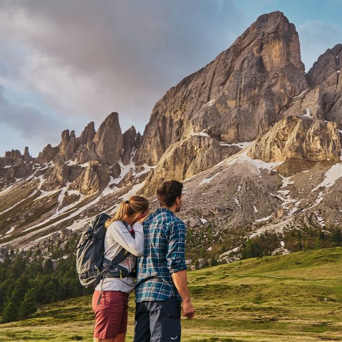 Couple with backpacks standing together in front of a mountain at Falkensteiner Hotel Kronplatz