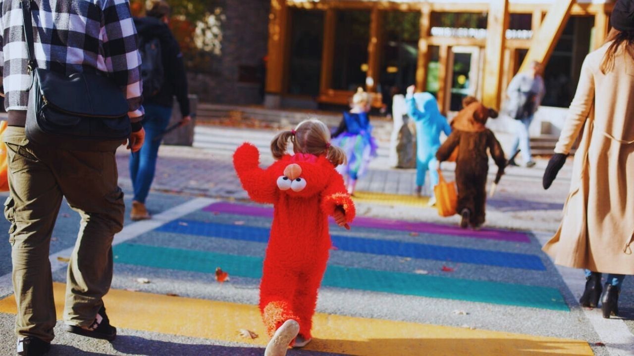 A child in an Elmo costume walks on a colorful crosswalk with other children.