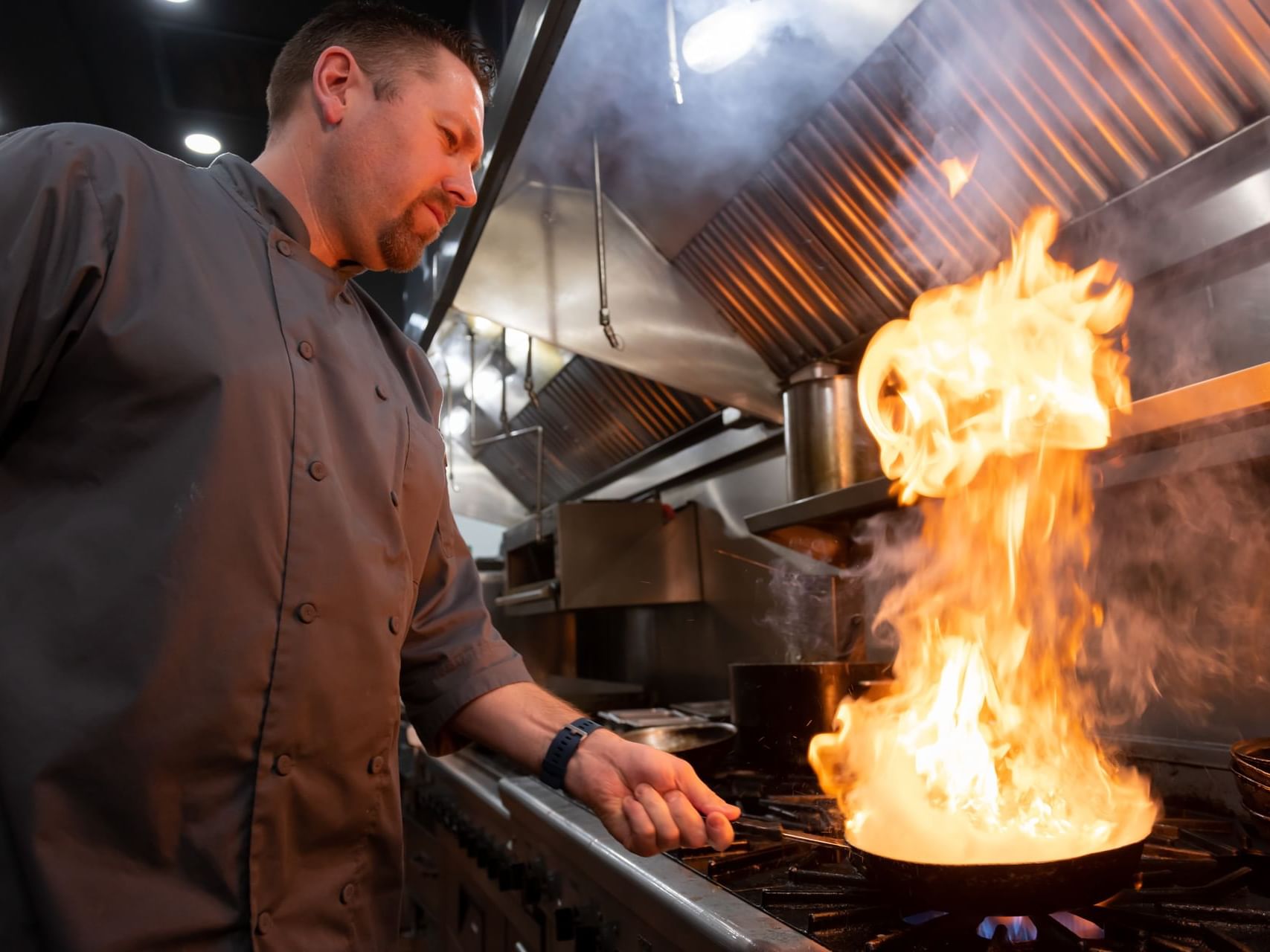 Chef cooking on a stove with flames in the Fort McMurray restaurants at Merit Hotel & Suites