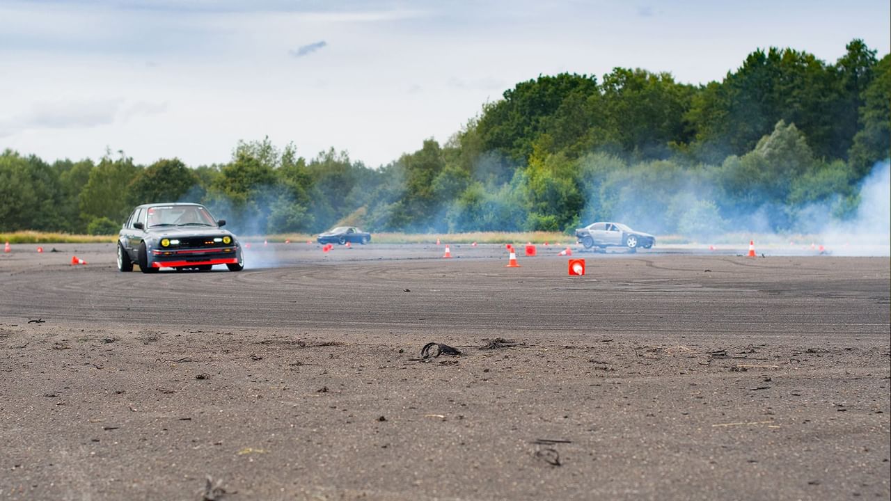 Black car drifting around a turn on a gravel track, surrounded by smoke at Penticton Speedway near Coast Penticton Hotel