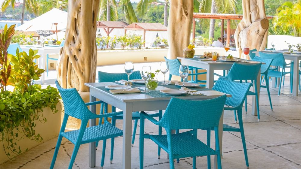 Club de Playa La Cuija restaurant at Quinta Real Huatulco, featuring teal wicker chairs by a wooden table in blue colour