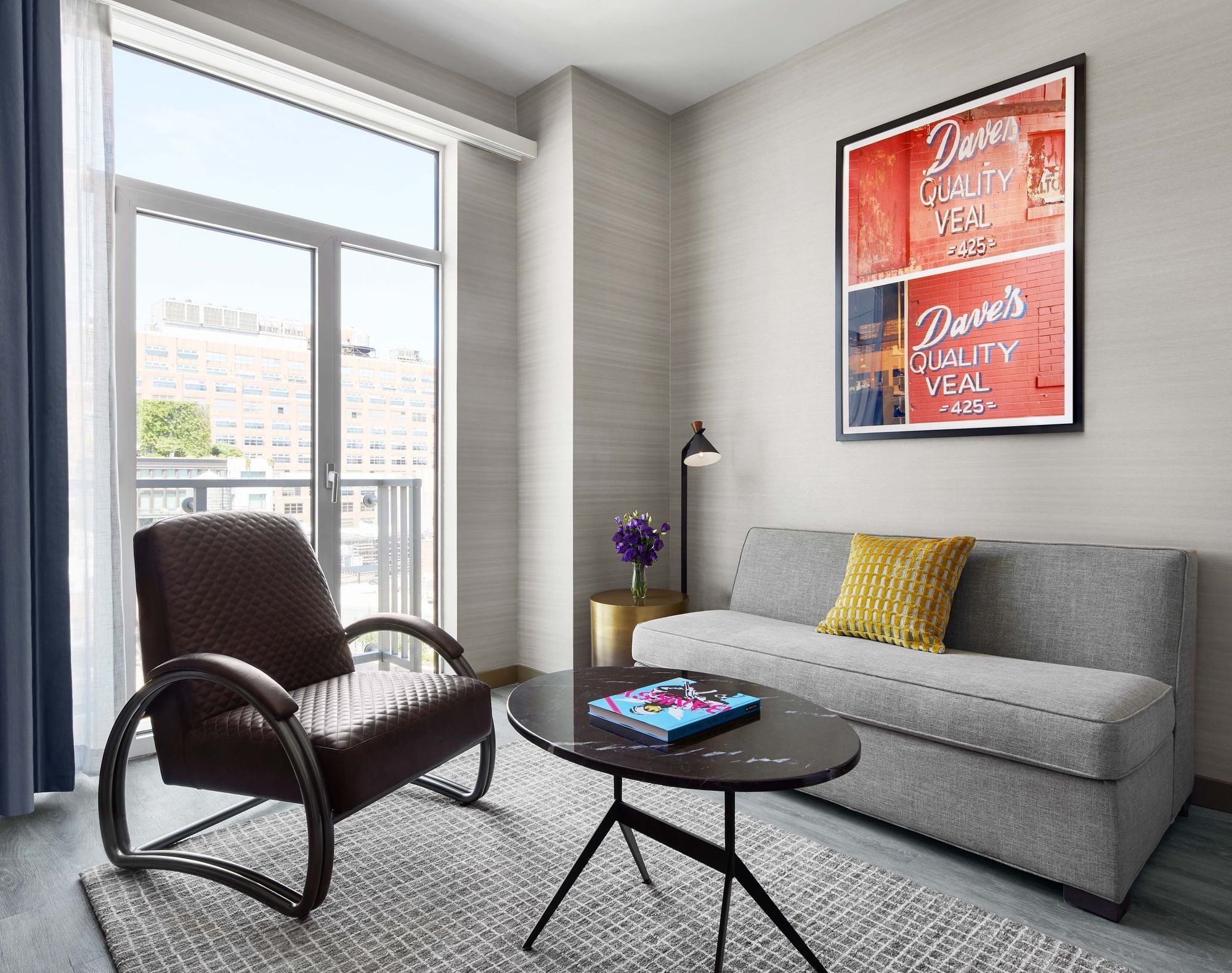 Suite living room area with couch, chair and juliet balcony with art on the wall showcasing the Meatpacking District