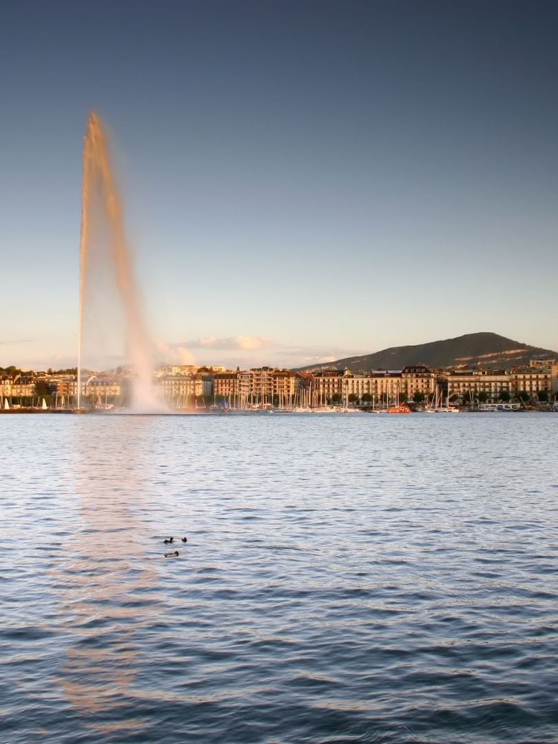 Jet d'Eau with a tall water fountain by a city skyline under a clear evening sky