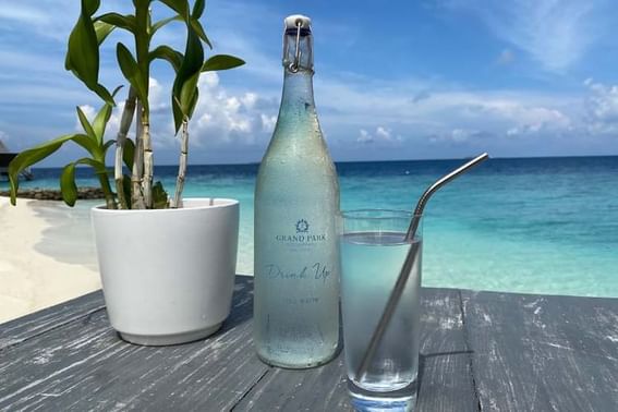 A close-up of a table by the ocean holds a bottle of water and a glass at Grand Park Kodhipparu, Maldives