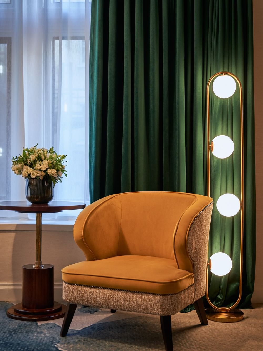 Elegant Deluxe Room with an armchair, table, and modern lighting at The Capital Hotel