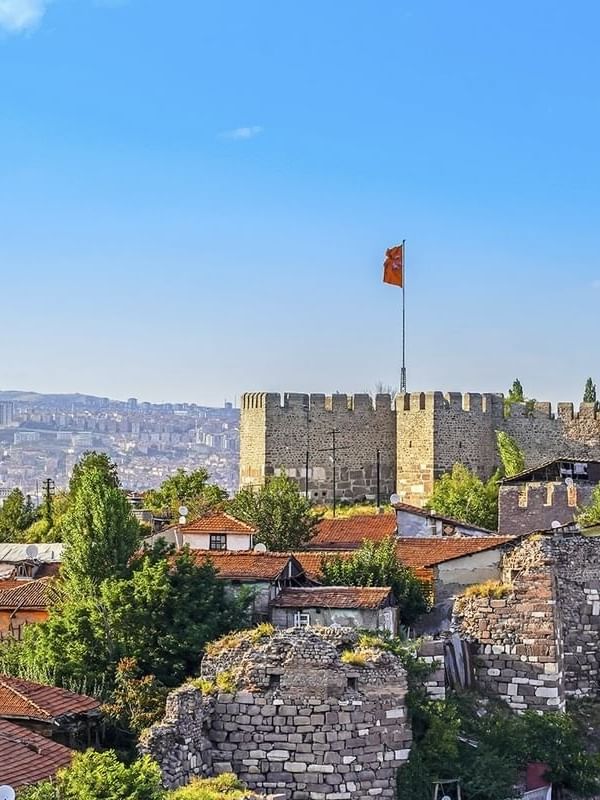 Ankara Castle walls by red-roofed houses surrounding a tall flag pole near Warwick Ankara