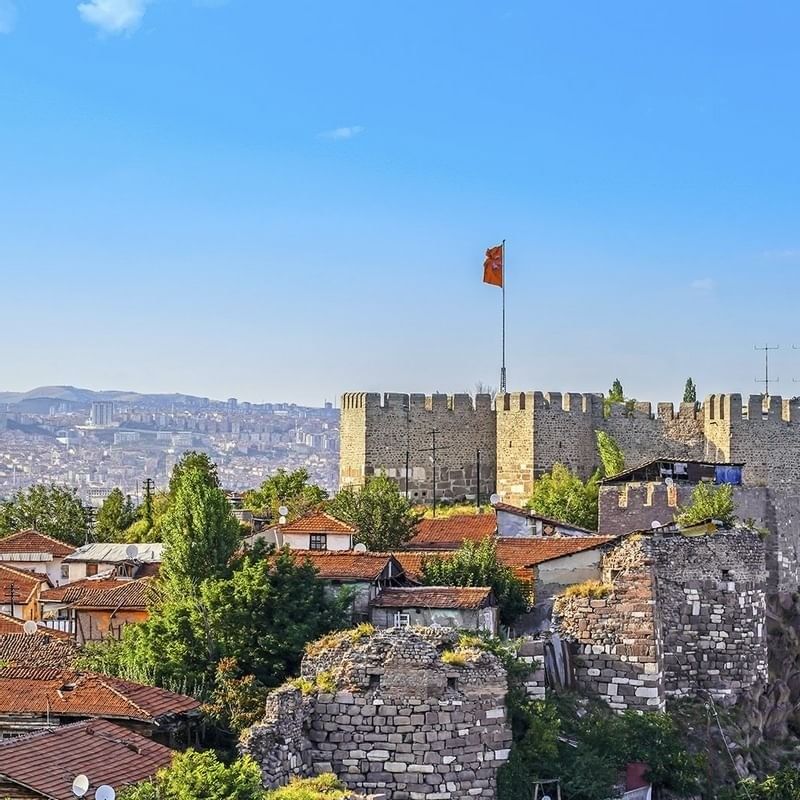 Ankara Castle walls by red-roofed houses surrounding a tall flag pole near Warwick Ankara