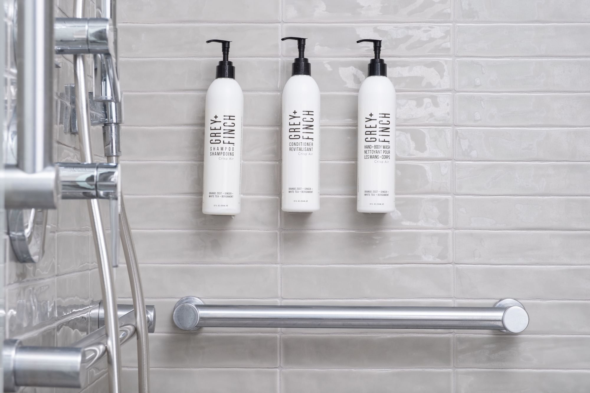 Three shampoo bottles on a tiled bathroom wall next to a shower and grab bar.