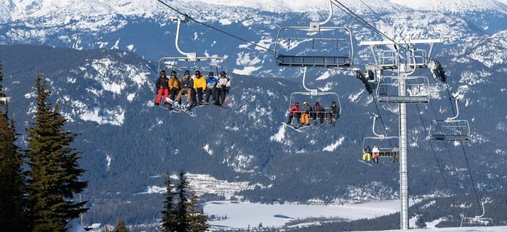Skiers riding chairlift above snowy Whistler mountains