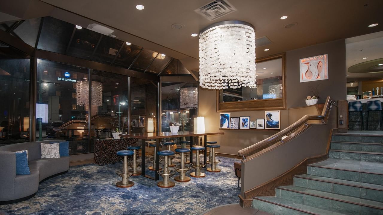 Lounge area with bar, stools, chandelier, and staircase at Coast Bastion Hotel.
