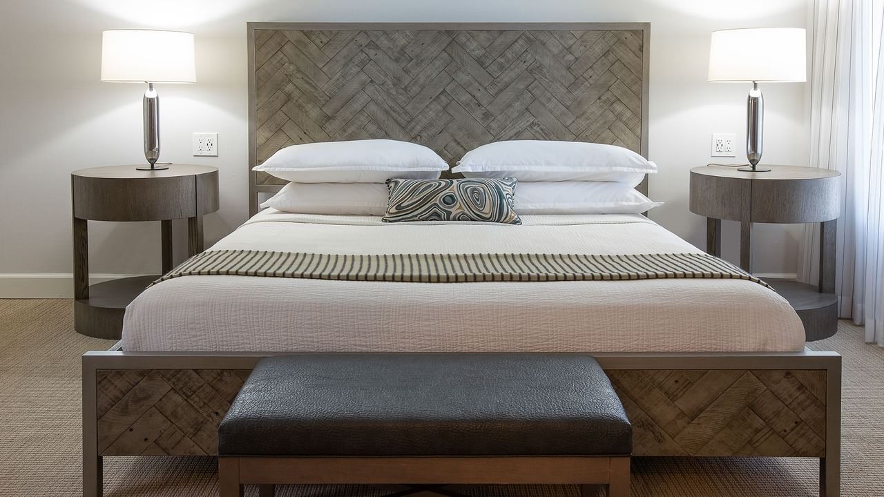 A neatly made bed with pillows and a blanket, flanked by nightstands with lamps.