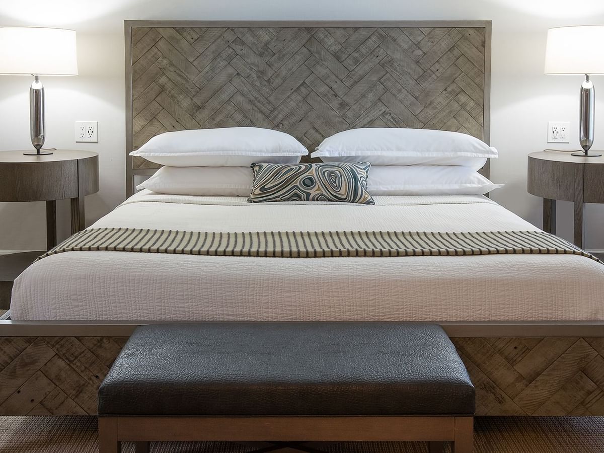 A hotel bed with a patterned headboard, white sheets, pillows, and nightstands with lamps on both sides.