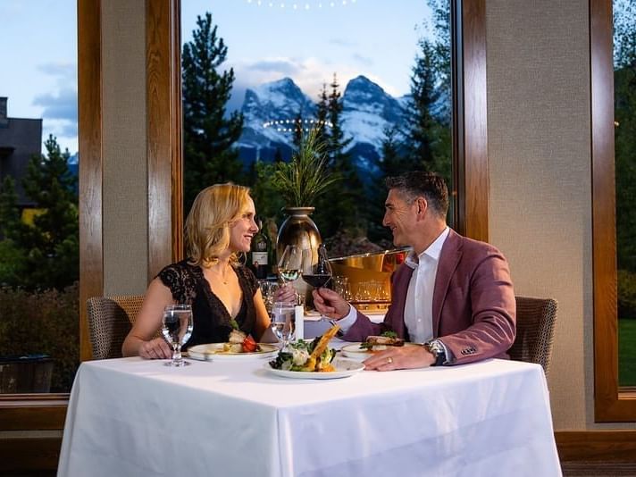A couple dining at a table with a mountain view, holding wine glasses, and smiling at each other at Spring Creek Resorts