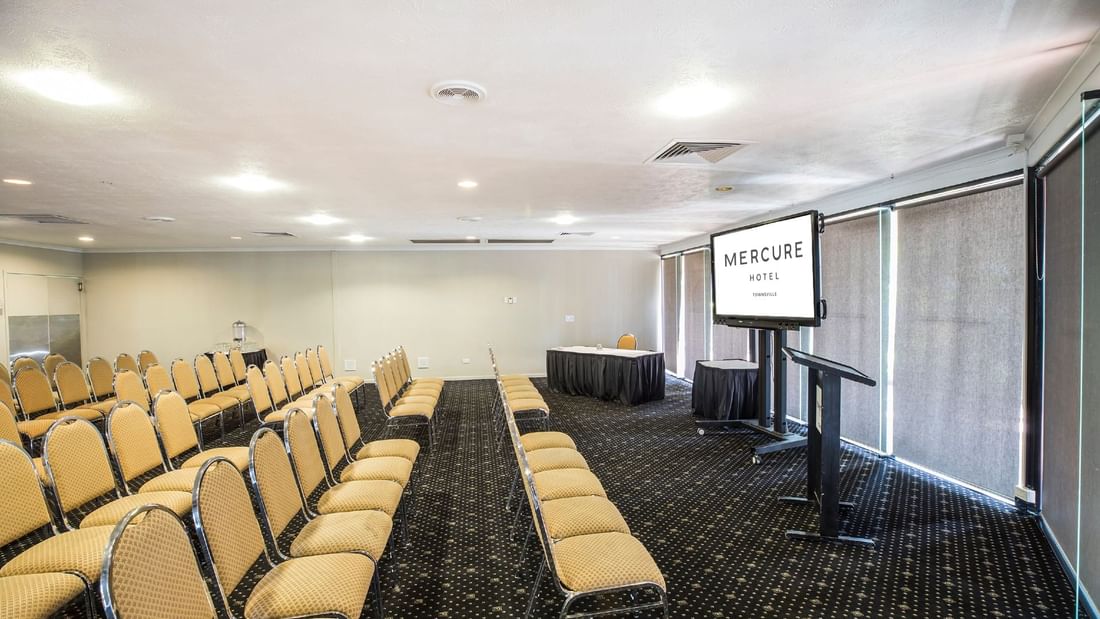 Rows of beige chairs, a display screen, and a speaker's podium in Lakes Room at Mercure Hotel Townsville