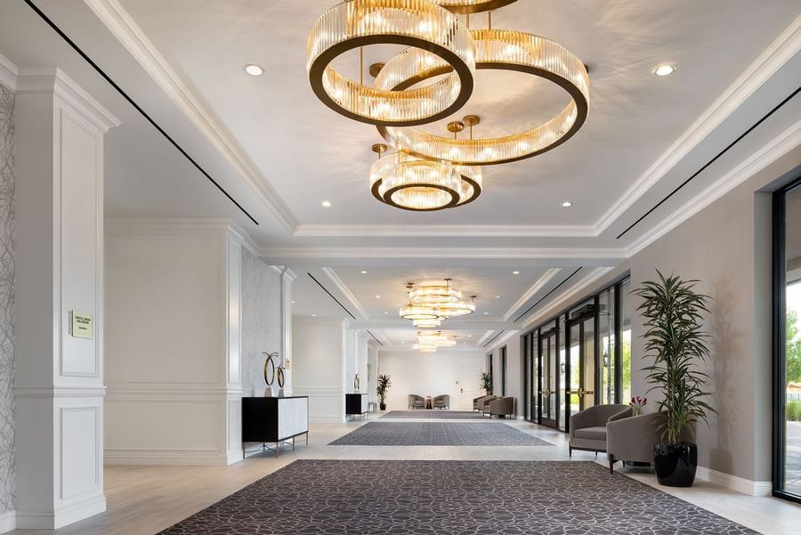 Grand hallway with grey carpets by armchairs under large circular chandeliers at Warwick Melrose Dallas