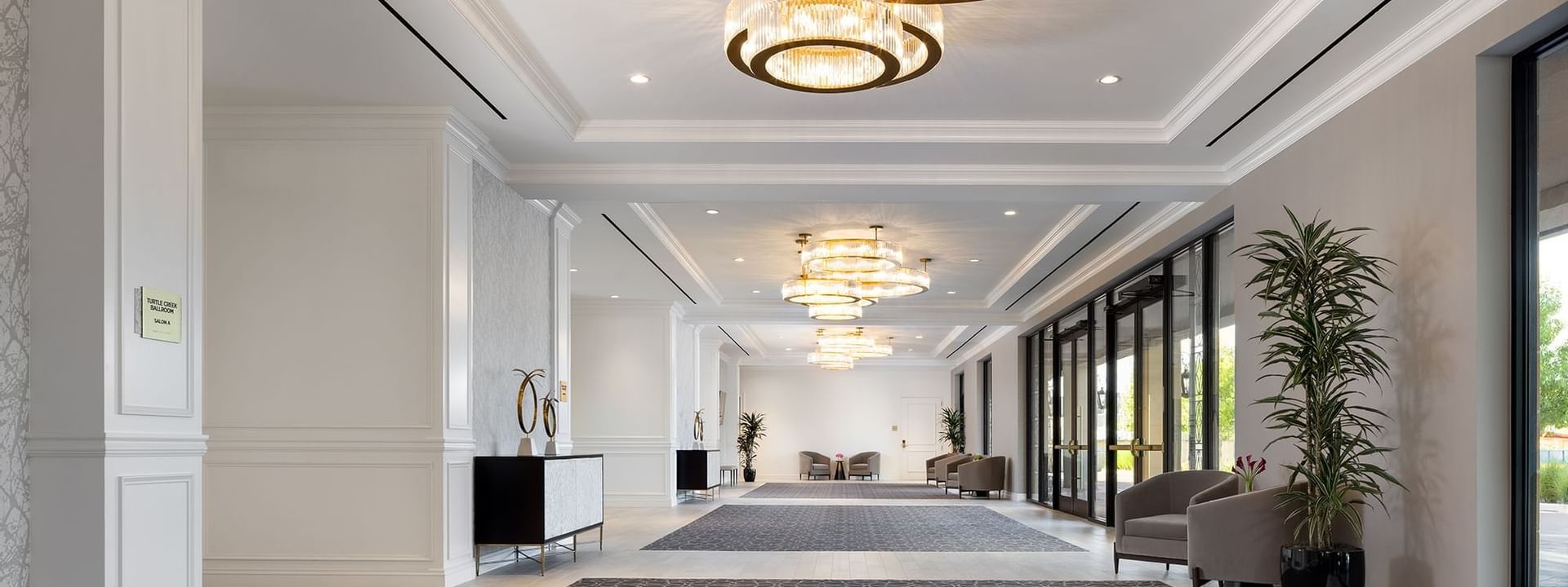 Long hallway with grey carpets by armchairs under large circular crystal chandeliers in The Foyer at Warwick Melrose Dallas