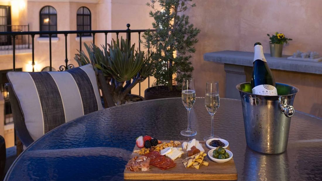 A tempting charcuterie board, champagne, and glasses set on a charming outdoor terrace in penthouse at El Prado Hotel
