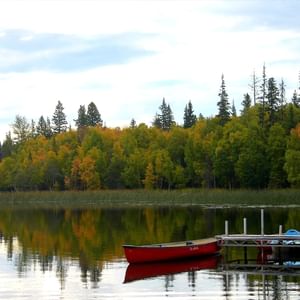 Canoe docked at a wooden pier on a serene lake reflecting fall colors of the surrounding trees.