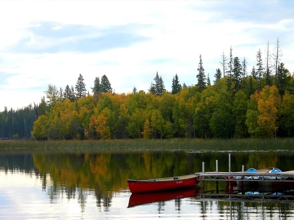 Canoe docked at a wooden pier on a serene lake reflecting fall colors of the surrounding trees.