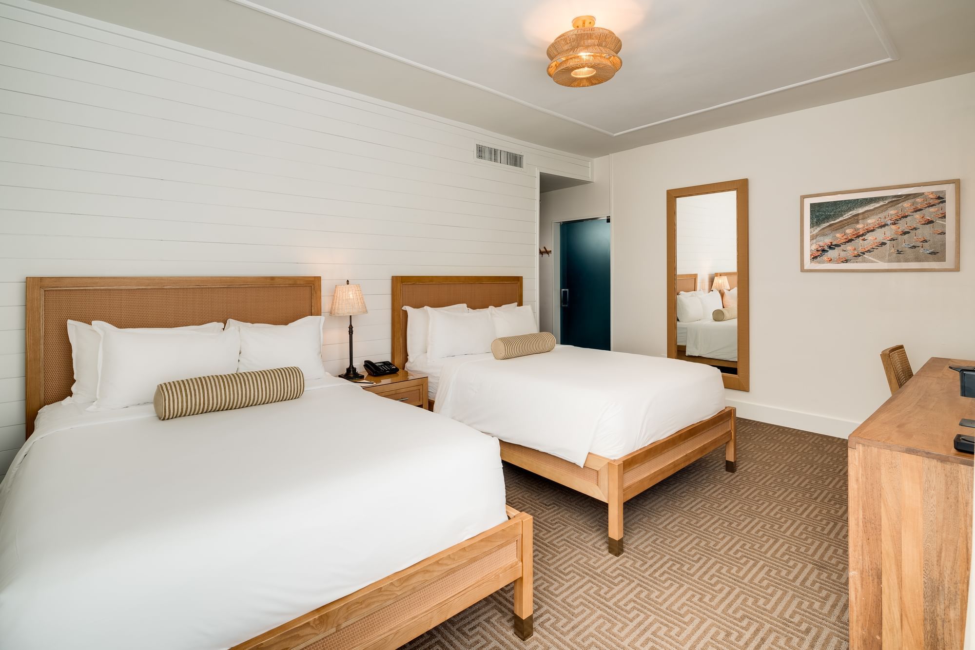 A hotel room with two twin beds, a desk, and a mirror.