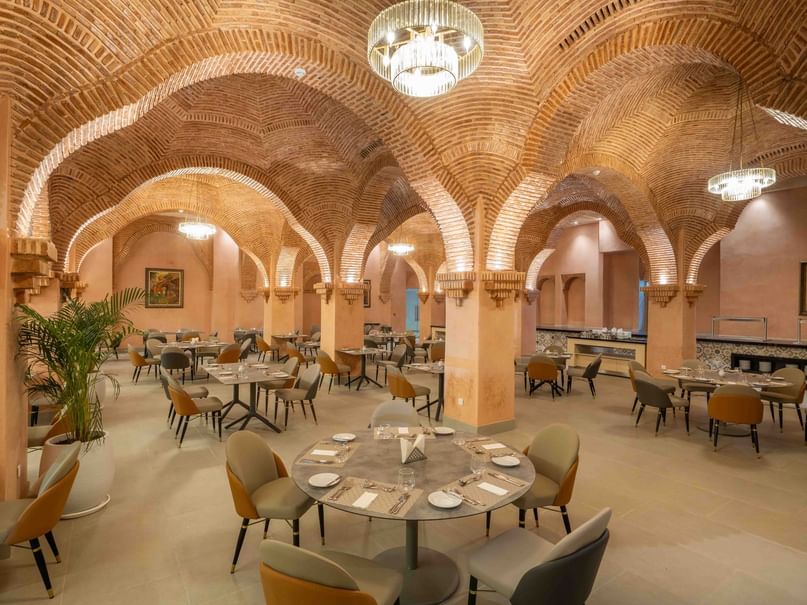 A well-furnished restaurant with arched ceilings, round tables, and modern chairs under hanging lights.