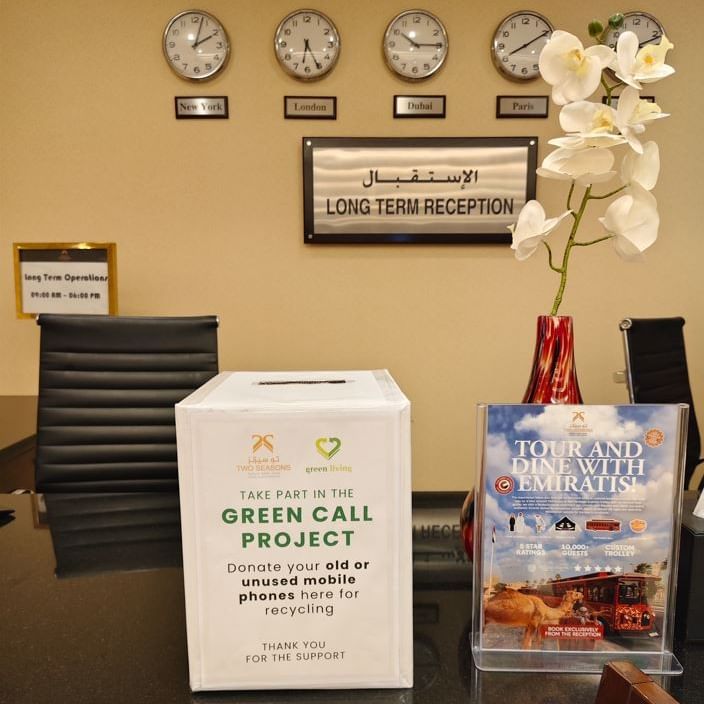 White box and a pamphlet on a table in front of a reception desk with clocks.
