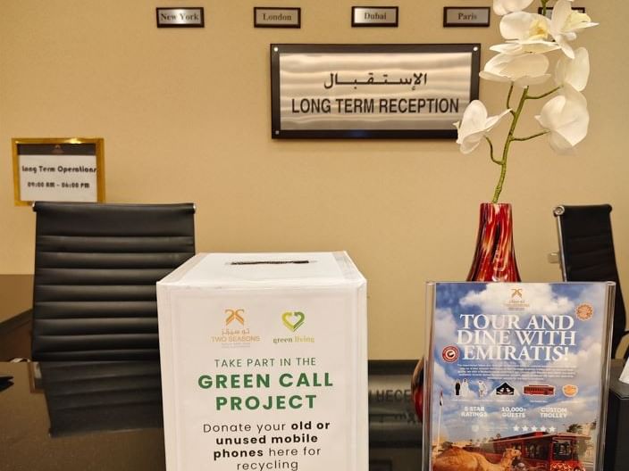 Weiße Schachtel und eine Broschüre auf einem Tisch vor einem Empfangstresen mit Uhren.