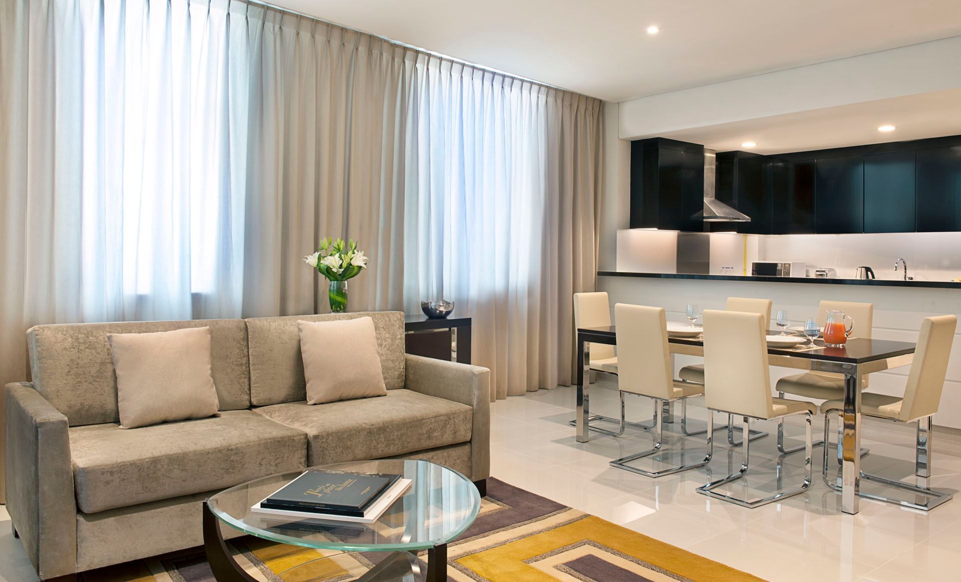 Modern living room with a sofa, glass table, and open kitchen with dining area in Two Bedroom Suite at DAMAC Maison Cour Jardin