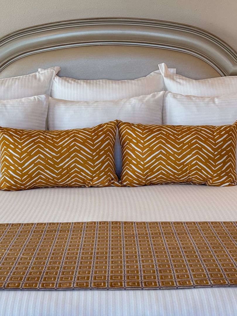 Corner King features White bed with yellow pillows by a silver headboard under soft light at Warwick Melrose Dallas