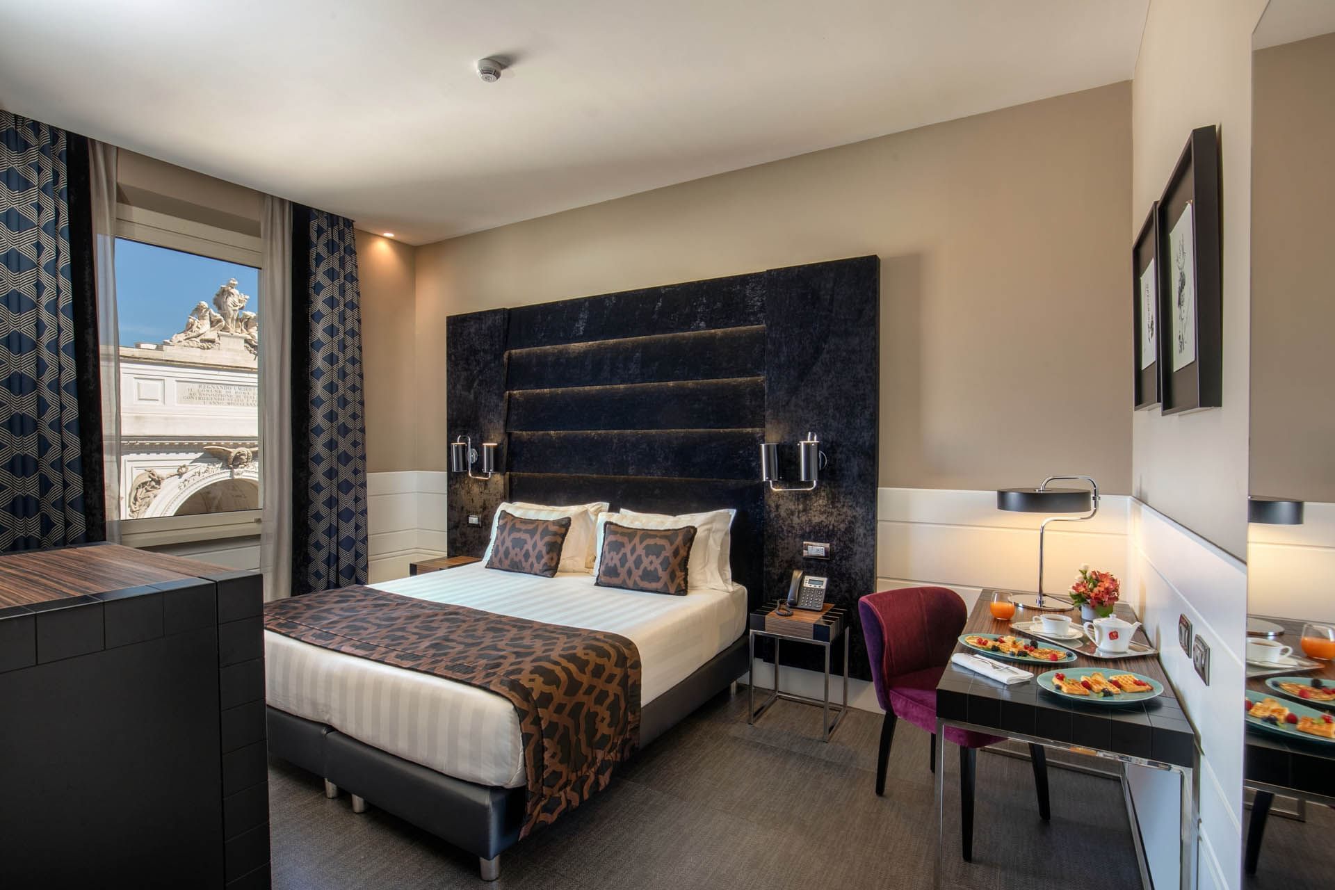 Bed beside a desk with a breakfast setup and large windows offering a scenic view in the Superior Room at The Glam Hotel