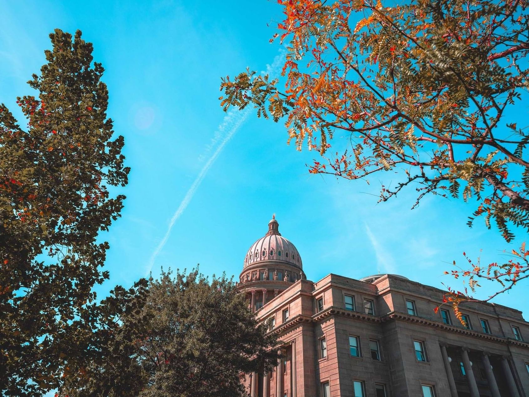 A view of the dome of the Idaho State Capitol Building near Hotel 43 Boise framed by colorful autumn leaves and a bright sky