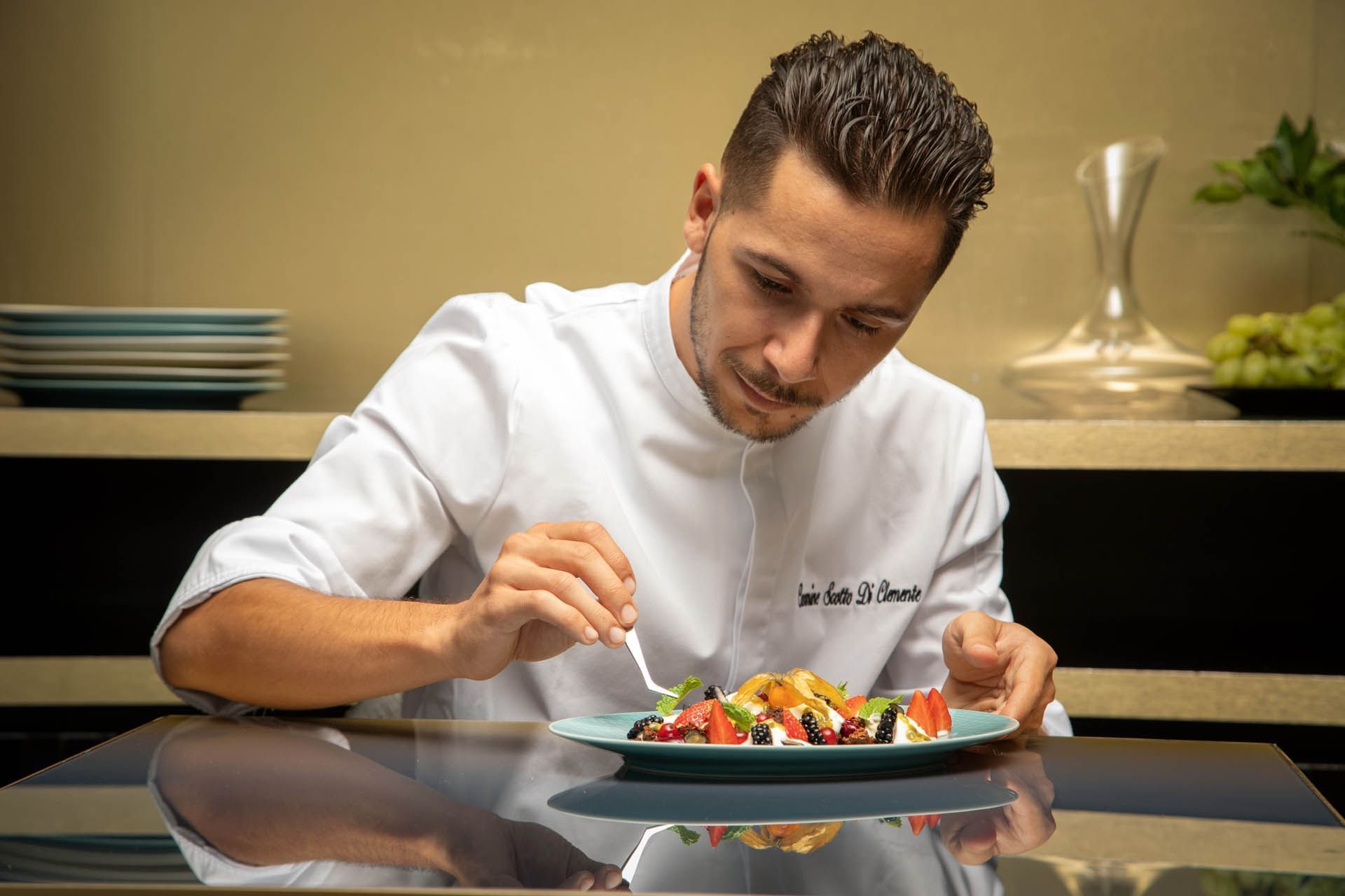 Chef decoratively arranging a vibrant fruit dessert on a plate at The Glam Hotel
