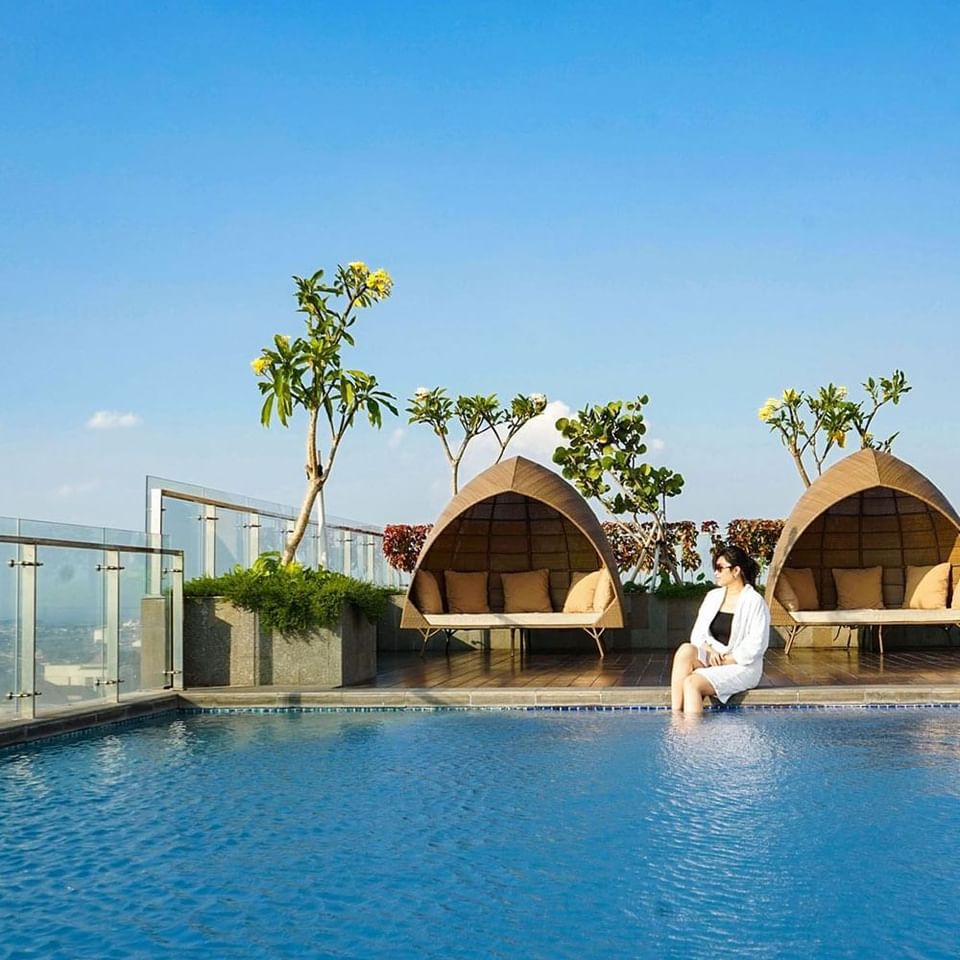 A lady sitting next to the rooftop pool at LK Pemuda Semarang Hotel & Residences