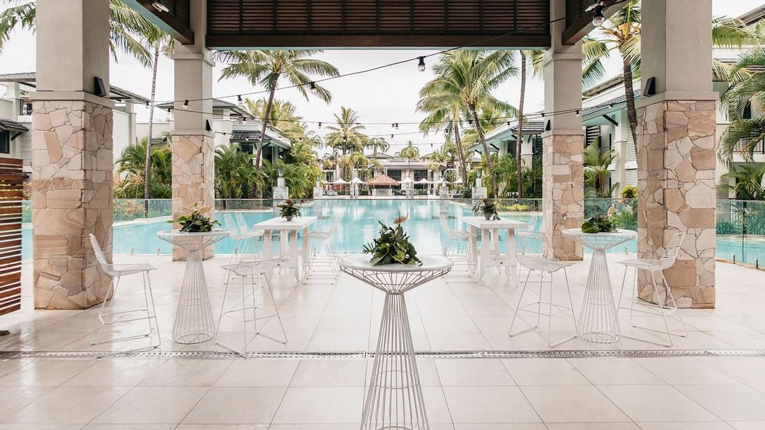 Poolside area with chairs & tables surrounded by plants & palm trees in Lagoon View Terrace at Pullman Port Douglas