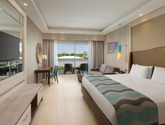 Spacious suite with king bed, seating area, and balcony overlooking pool at Titanic Deluxe Golf Belek, Antalya