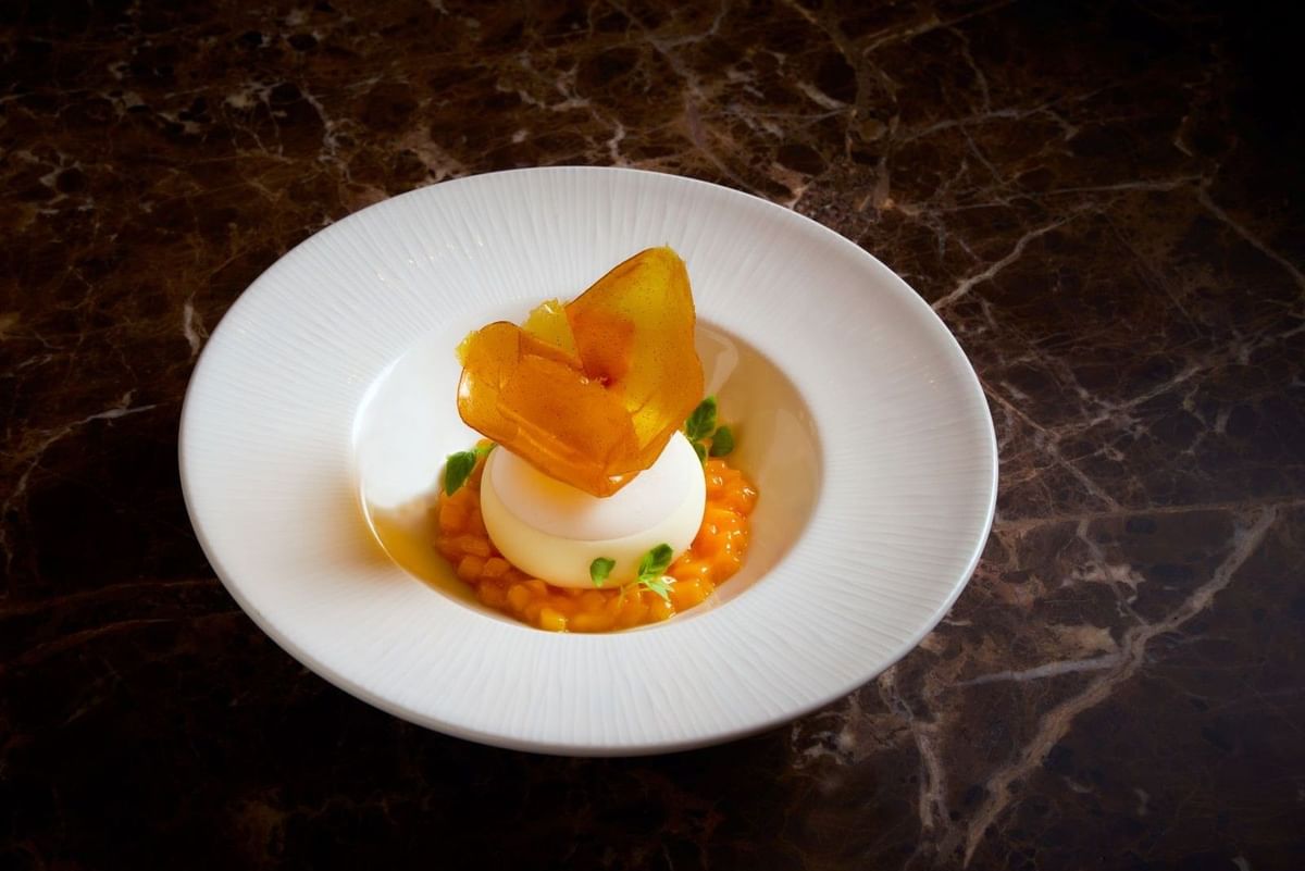 Gourmet white chocolate mousse dessert served with diced mango on a dark marble table at The May Fair Hotel