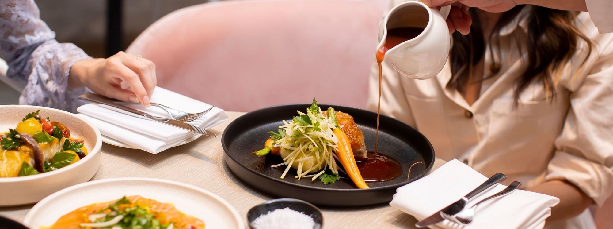 Close-up of a person pouring sauce onto a beautifully plated dish at Novotel Sydney International Airport