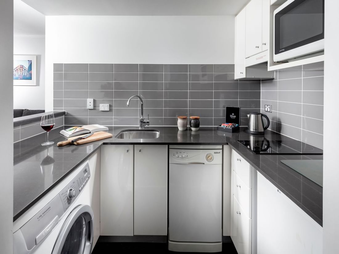 Kitchenette with a washing machine, dishwasher, cooktop, and microwave in One Bedroom Apartment at The Sebel Brisbane