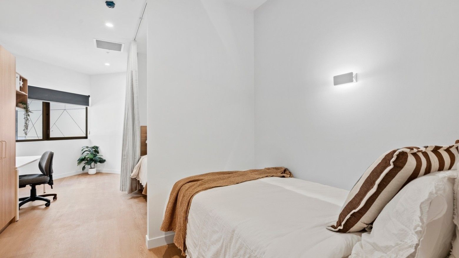 Cozy bedroom with white walls, wooden floors, and simple decor at UniLodge Brisbane City.