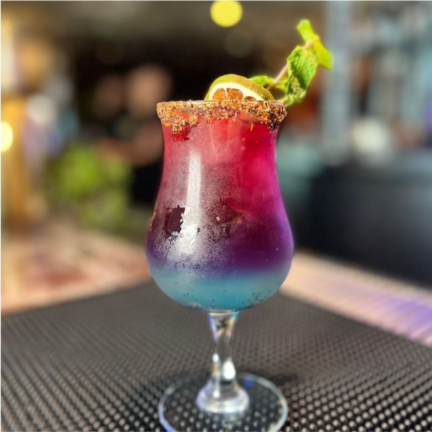 Cóctel en capas rosas, moradas y azules con borde especiado, lima y menta en el bar de Megapolis Hotel Panama