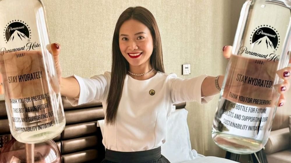 Smiling staff member promoting sustainability, holding large reusable water bottles at Paramount Hotel Dubai