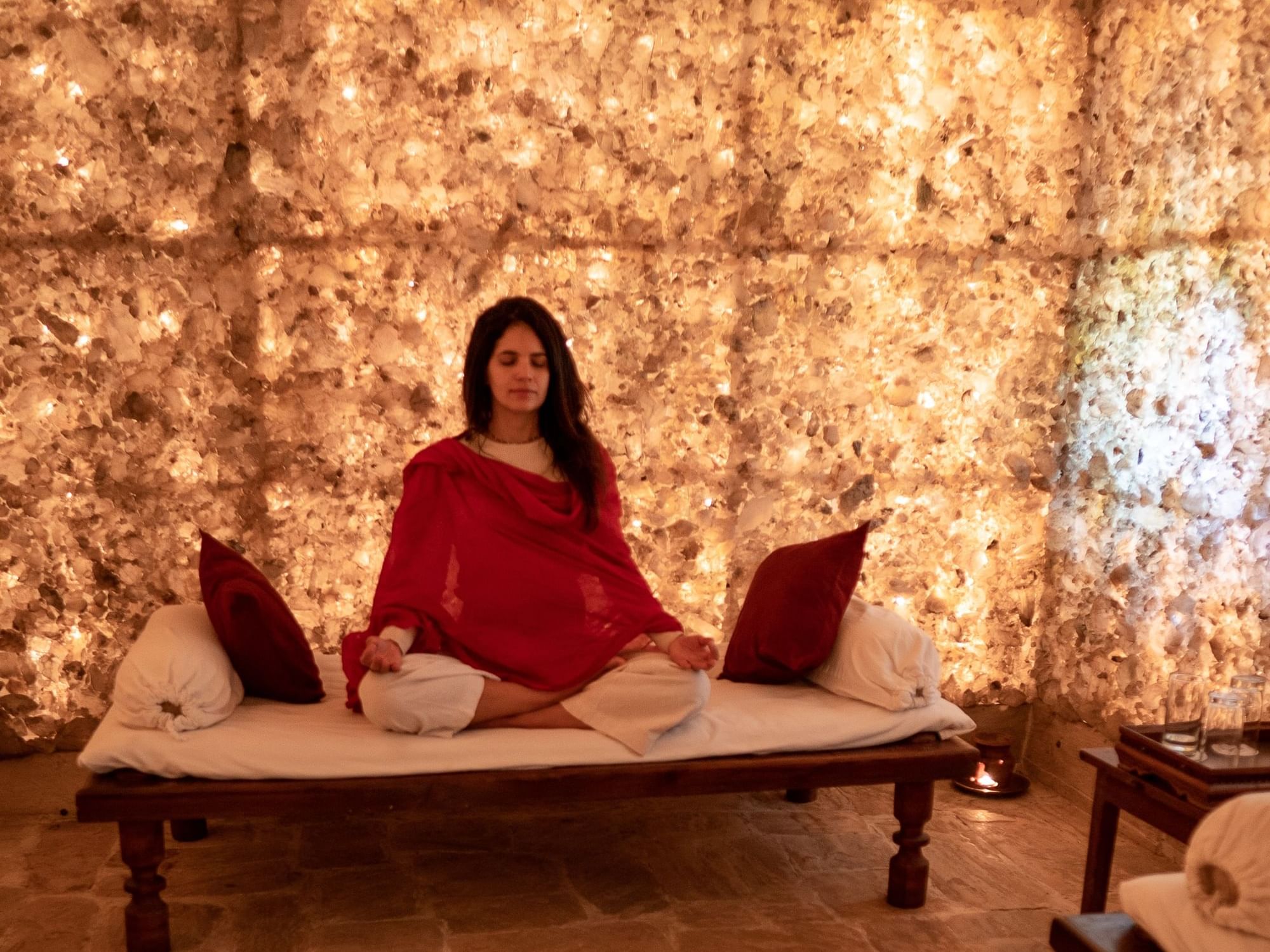 Lady in red robe meditating on a bed surrounded by a glowing salt wall at Dwarika's Himalayan Wellbeing
