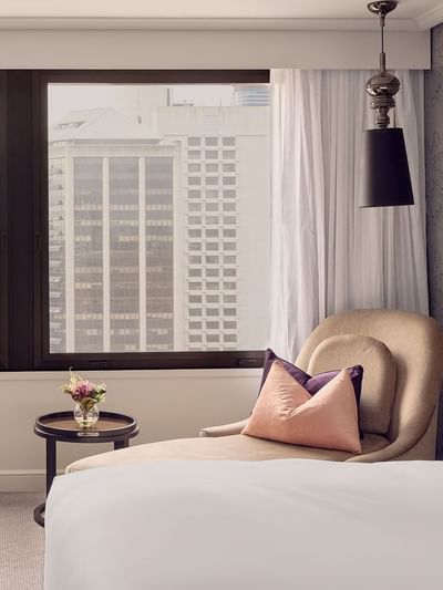 Luxury hotel room with city view from large window and comfortable seating area.