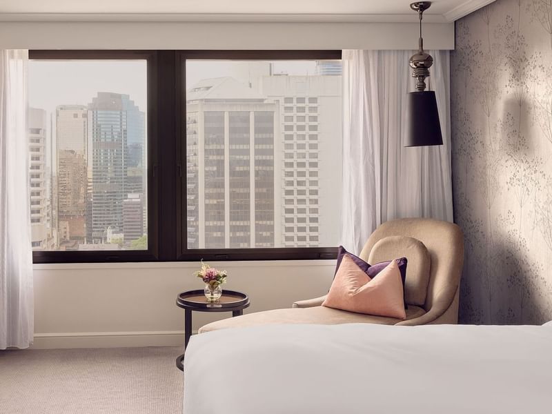 Luxury hotel room with city view from large window and comfortable seating area.