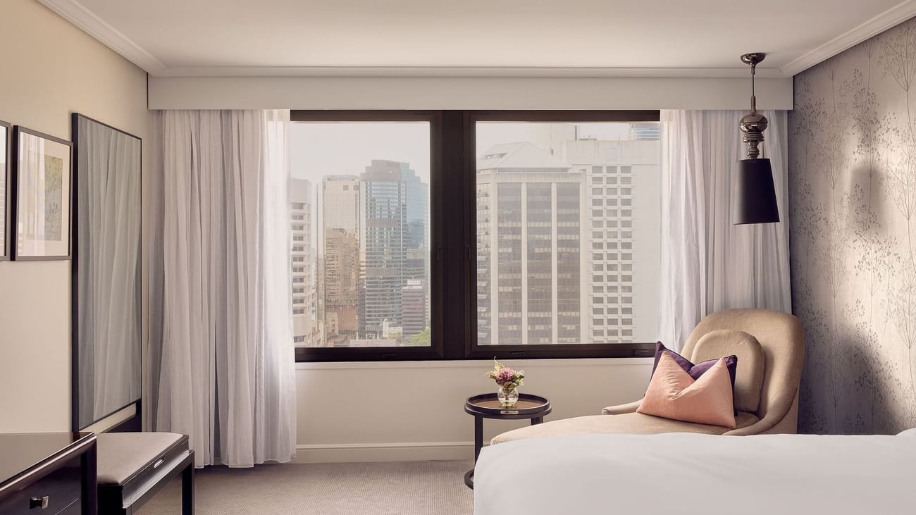 Luxury hotel room with city view from large window and comfortable seating area.