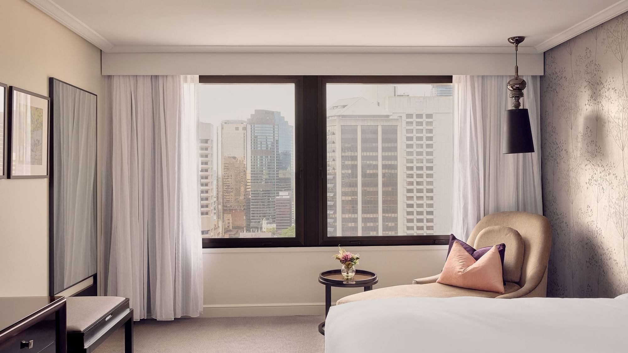 Luxury hotel room with city view from large window and comfortable seating area.