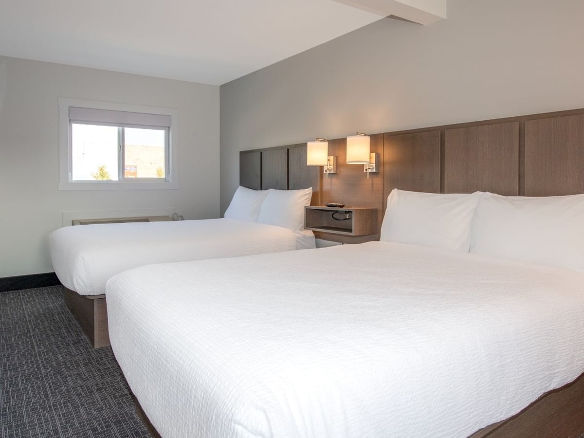 Two beds with white bedding, a TV, and two lamps in a modern hotel room.