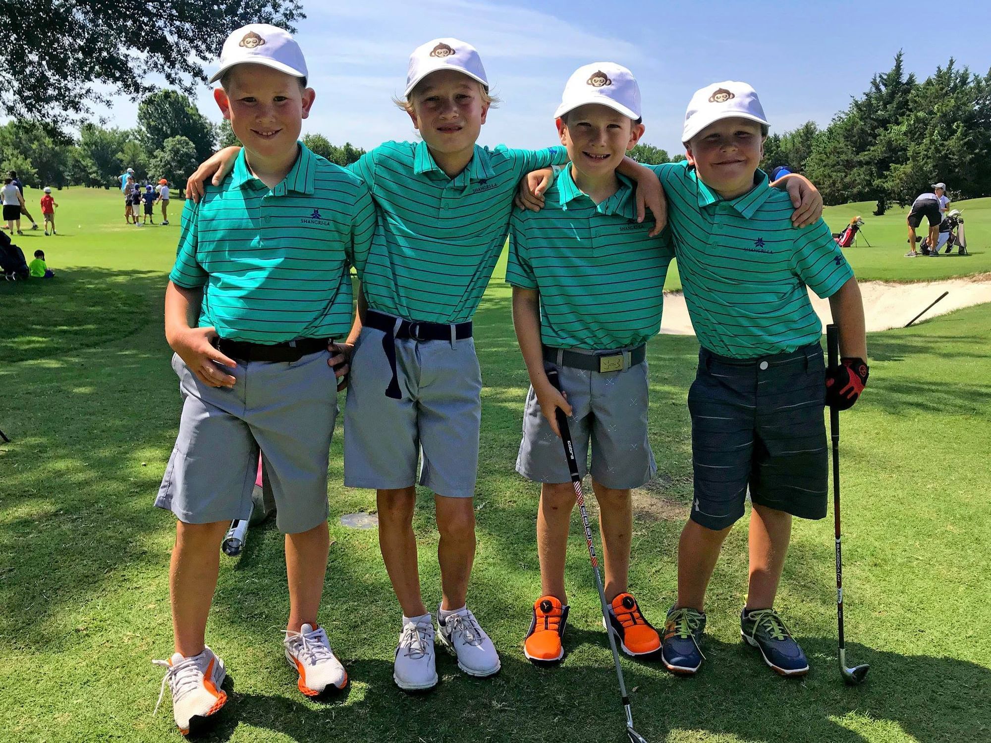Four young boys in matching teal striped golf shirts and white hats pose on a green at Shangri-La Resort and Golf Club