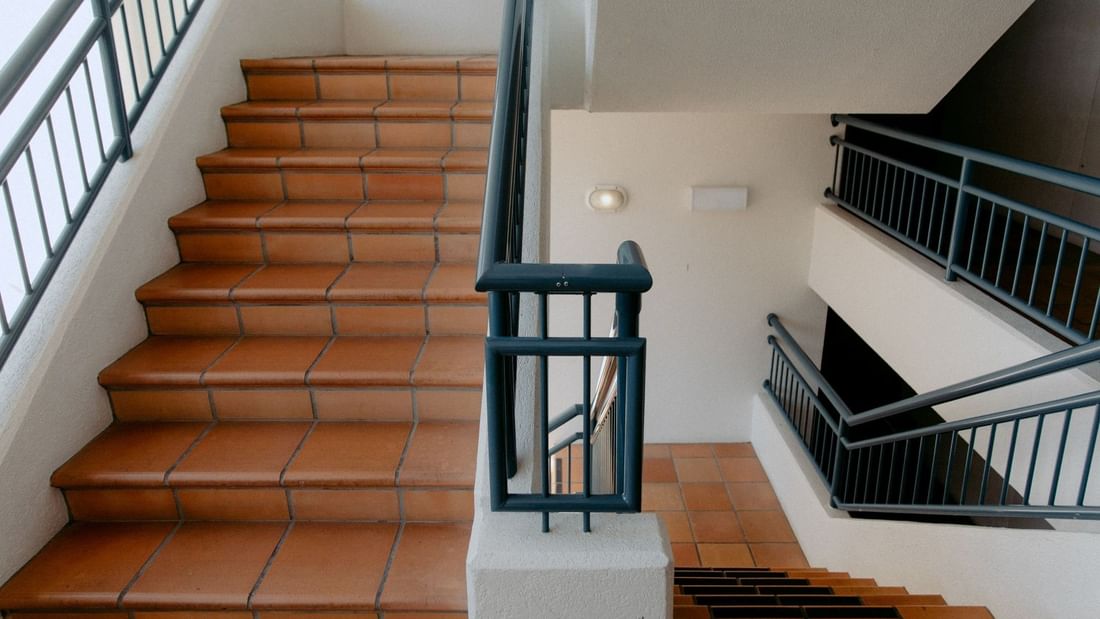 Stairs with brown tiles and black railings leading up to a second-floor landing with another set of stairs.